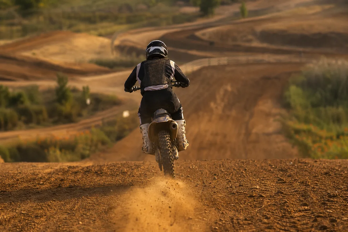 Pilote de motocross vu de dos réceptionnant un saut sur la descente d’une table en terre